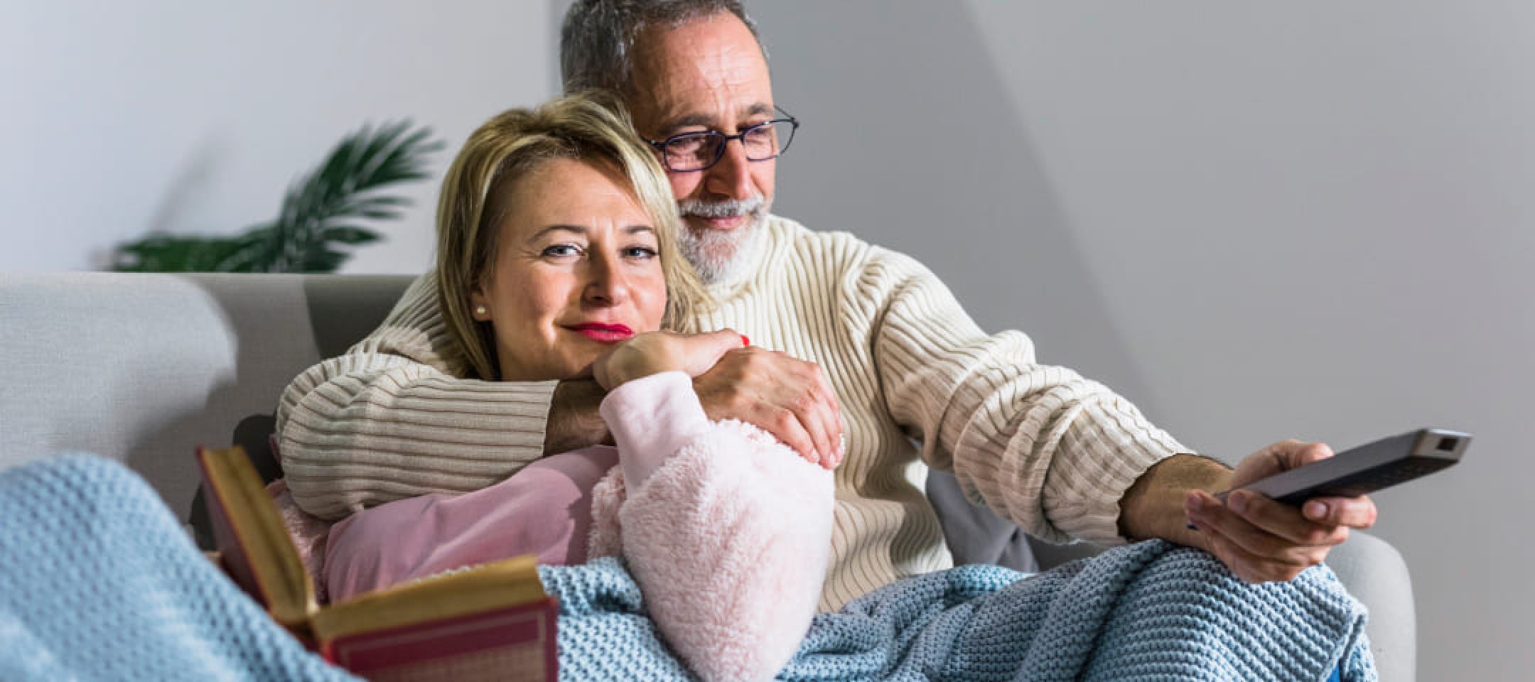Photo of a man and a woman sitting on a couch; the man is pointing a remote control